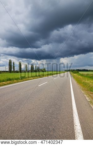 Empty Highway, Paved Road Through The Fields. Dramatic Sky, Rain On The Horizon In The Distance. The