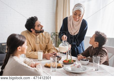 African American Woman In Hijab Pouring Milk Near Family During Suhur Breakfast At Home.