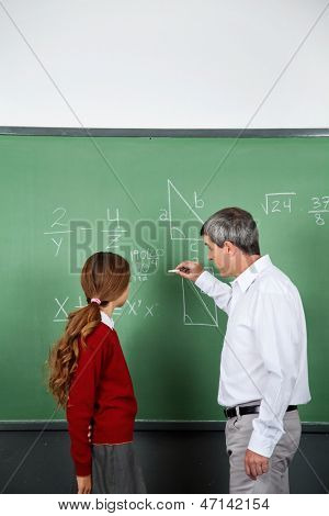 Sideudsigt over ældre mandlig lærer undervisning matematik til teenage pige i klasseværelset