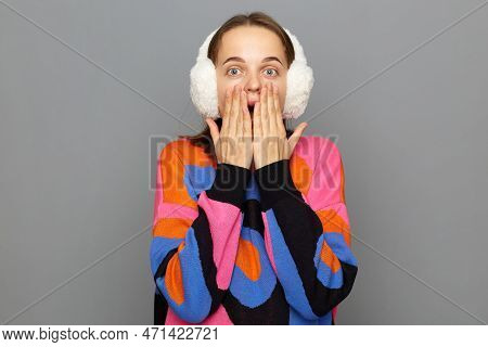 Wow. Photo Of Young Woman Wearing White Fluffy Ear Warmers And Colorful Sweater, Feeling Shocked And