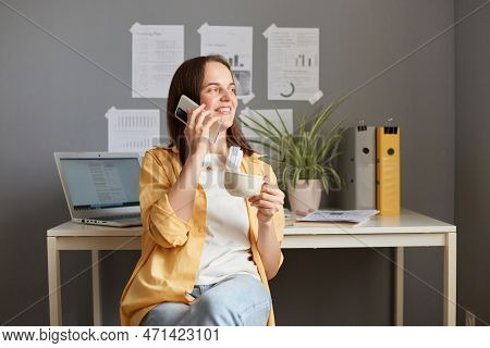 Horizontal Shot Of Adorable Beautiful Joyful Woman With Brown Hair Wearing Yellow Shirt Posing In Of