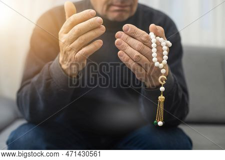An Elderly Man Prays With A Rosary And The Flag Of The United Arab Emirates