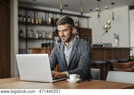 A Bearded Businessman Is Sitting In A Working Friendly Cafe And Working On An Important Project. A B