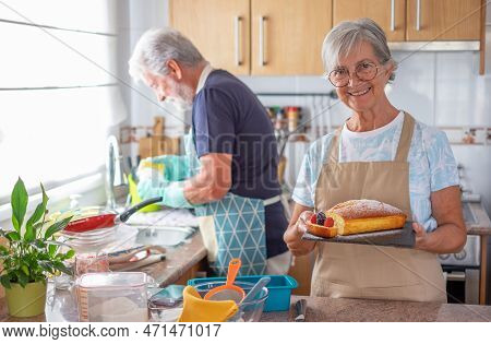Elderly Caucasian Woman In The Home Kitchen Proudly Displays A Freshly Baked Homemade Plumcake Serve
