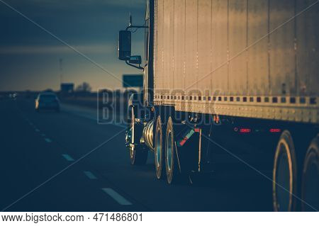 Back View Closeup Of American Semi Truck On The Road Driving Forward In Sunset Rays. Transportation 