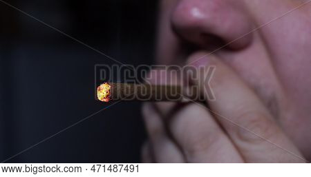 Close-up. Man Puffing On A Cigarette. The Face Of A Man Smoking A Cigarette. A Red Ember Glows In Th