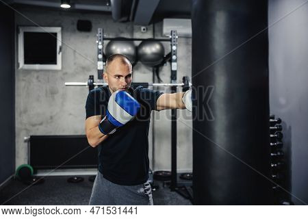 Boxing Training. Male Boxer Hitting A Black Punching Bag At A Fitness Studio. Male Adult Boxer Weari