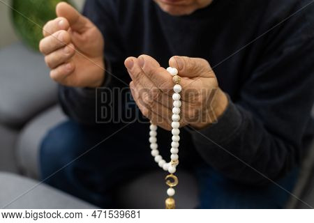 An Elderly Man Prays With A Rosary And The Flag Of The United Arab Emirates