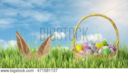 Bunny Hiding Near Wicker Basket Full Of Easter Eggs In Green Grass On Sunny Day