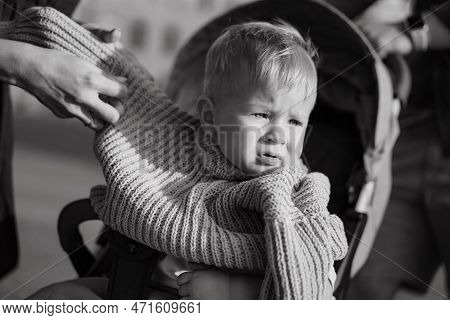 Cute Caucasian Baby Boy Sitting In A Stroller. Mother Is Putting A Swaeter On Him.image With Selecti