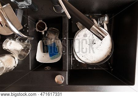 Washing Dishes Concept. Dirty Dishes With Foam From Detergent In A Black Stone Sink In The Kitchen T