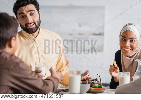 Smiling Muslim Parents Talking To Son Near Suhur Food At Home.