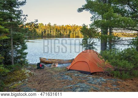 Campsite With Orange Tent And Canoe On Northern Minnesota Lake At Sunrise During Autumn