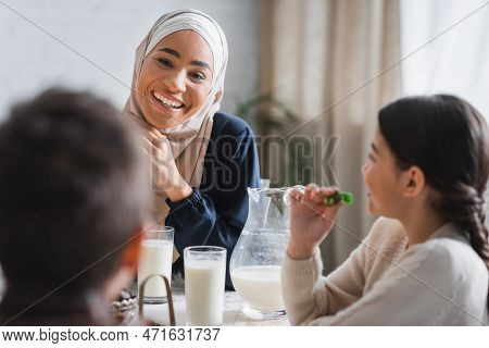 Smiling African American Mother In Hijab Looking At Blurred Children Near Suhur Food At Home.