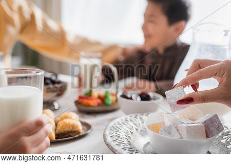Muslim Woman Holding Turkish Delight Near Suhur Food And Blurred Family At Home.