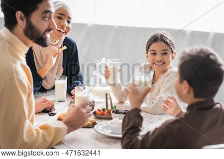 Positive Muslim Family Holding Glasses Of Milk And Talking Near Food During Suhur At Home.