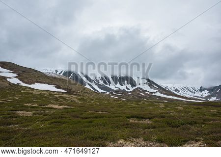 Dramatic Alpine Landscape With Snowy Mountains In Gray Low Clouds. Bleak Atmospheric Scenery Of Tund