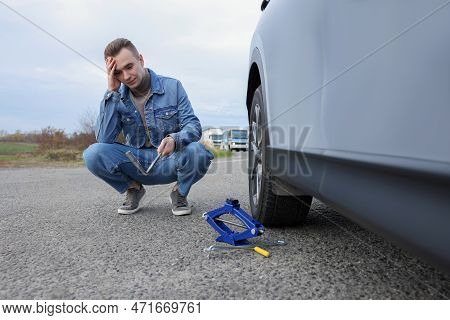 Worried Young Man Near Car With Punctured Wheel On Roadside