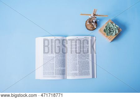 Open Holy Bible With Cross And Decorative Flowers On Blue Background. Flat Lay
