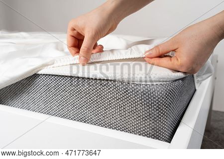 A White Satin Sheet With An Elastic Band Is Put On The Mattress Of The Bed, A Close-up Of The Hands.