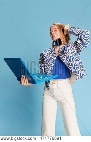 Dj. Delightful Young Smiling Girl In Headphones And Laptop Over Blue Studio Background. Listening An