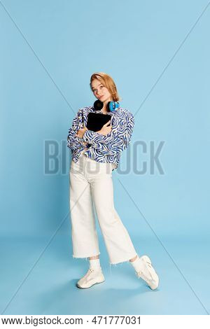 Full-length Portrait Of Beautiful Young Girl In Headphones, With Laptop Posing Over Blue Studio Back