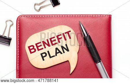 On A Light Background There Are Black Paper Clips, A Pen, A Burgundy Notepad A Wooden Board With The