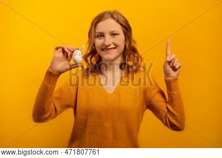Happy Smiling Young Woman In Yellow Sweater Shows White Decorated Egg With Pink Rabbit Ears, Flowers