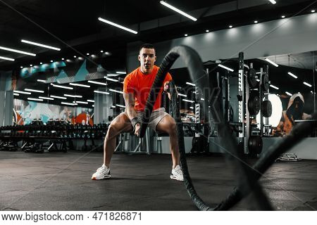 An Energetic Sportsman Is Doing Heavy Cardio Cross-fit Training With Battle Ropes In An Indoor Gym W