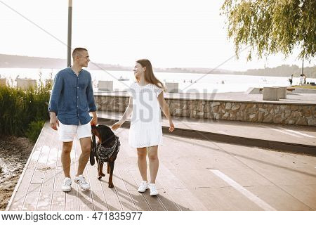 Portrait Of A Romantic Couple With Their Rotweiller Near The Lak