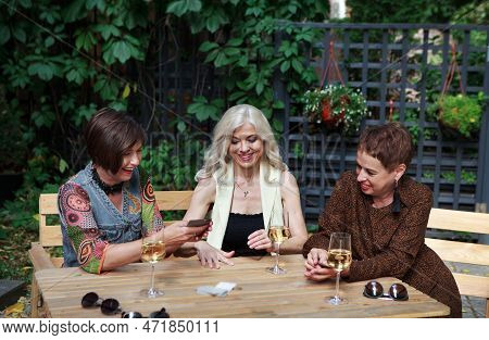Mature Female Friends Play Card Board Game In Cafe, Have Fun, Laughing And Drinking Wine From Bakals