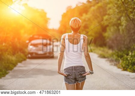 Young Sad Woman Standing Near The Road By The Broken Car In The Middle Of Nowhere. Smoke Coming Out