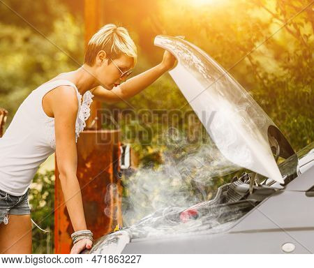 Young Sad Woman Standing Near The Road By The Broken Car In The Middle Of Nowhere. Smoke Coming Out