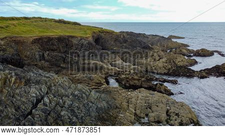 A Picturesque Stone Cape Covered With Green Grass. A Rock On The Seashore. The Rocky Coast Of The At