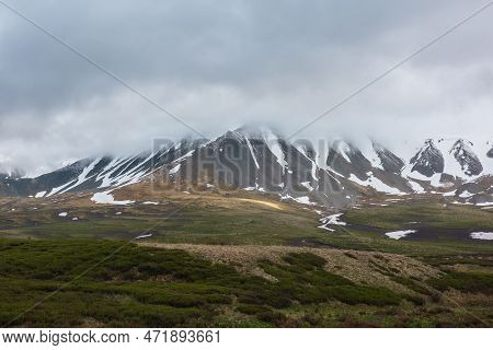 Dramatic Alpine Landscape With Snowy Mountains In Gray Low Clouds. Bleak Atmospheric Scenery Of Tund
