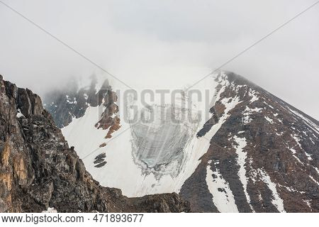 Atmospheric Landscape With Glacier On Rocky Mountain Top In Dense Low Clouds. Awesome Mountain Scene