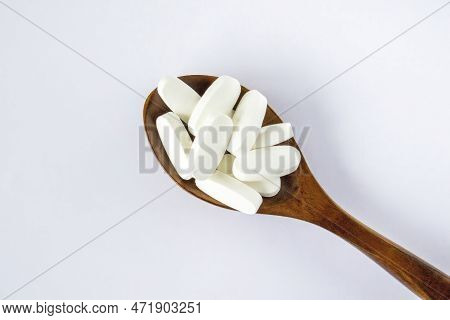 L Glutamine White Oval Tabletsin A Wooden Spoon On A White Background, Top View.