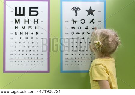 Little Girl At Appointment With Optometrist Near Poster To Check Her Eyesight. Pediatric Optometrist