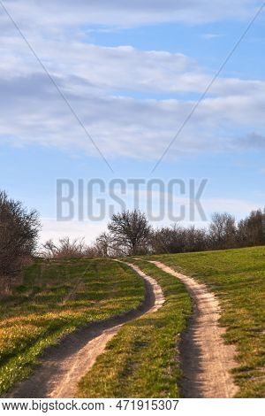 Dirt Rural Road Winding Across Countryside Highlands At The Border Of An Agricultural Field Under Bl