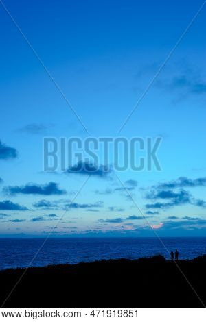 The Silhouette Of A Couple Viewing The Ocean At Twilight, As The Sea And Sky Turn A Dramatic Deep In