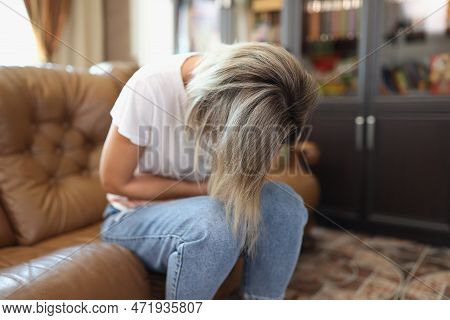 Portrait Of Female Sitting On Sofa, Touching Belly And Writhing In Pain. Stomachache, Menstrual Pain