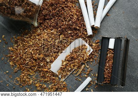 Flat Lay Composition With Roller And Tobacco On Dark Grey Table. Making Hand Rolled Cigarettes
