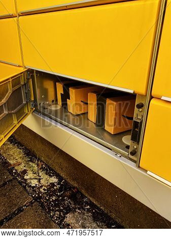 Cardboard Box In A Cell Postamat. Open Yellow Terminal Door. Post Automat Terminal And A Parcel In I