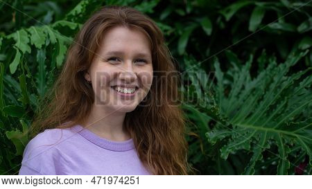 Portrait Of Young Woman Standing On An Ivy, Fern Wall Or In Greenery, Breathing, Smiling And Looking