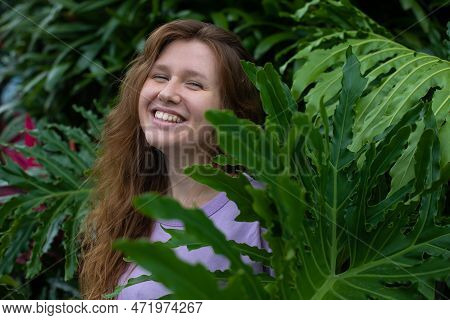 Portrait Of Young Woman Standing On An Ivy, Fern Wall Or In Greenery, Breathing, Smiling And Looking
