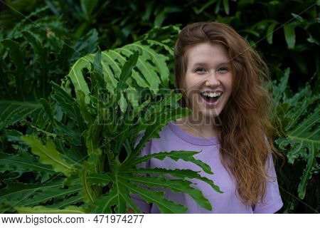 Portrait Of Young Woman Standing On An Ivy, Fern Wall Or In Greenery, Breathing, Smiling And Looking
