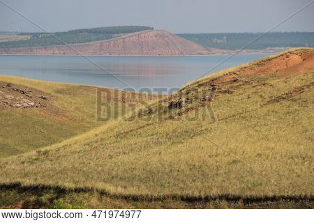 Rocky Hills And Ravine. Red Mountain On The Other Side Of The Lake.