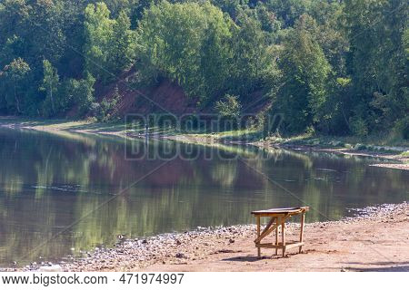A Wood Table Sitting On The Shore Of A Lake, Green Forest On Background