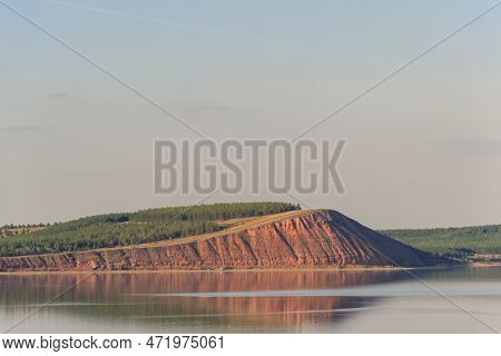 Lake With Clouds In The Sky, Red Hill With Forests On Background. Hill Symmetric Reflection In The W