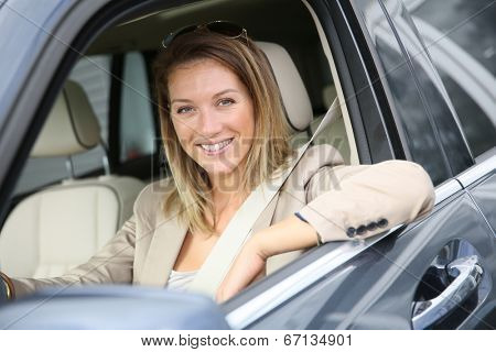 Cheerful woman at car window driving brand new vehicle